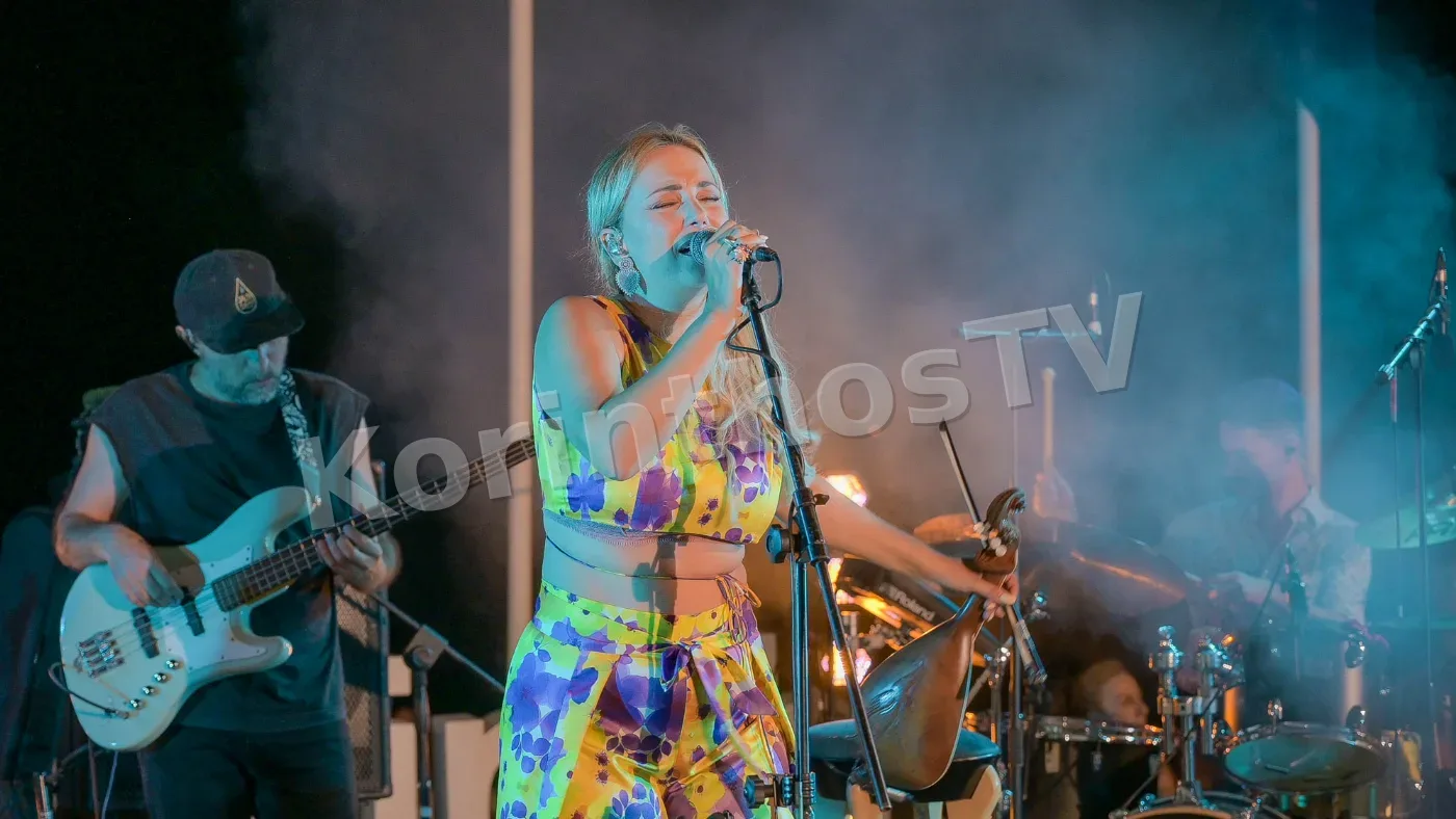 A singer performs passionately on stage, wearing a colorful outfit, with musicians playing instruments in the background amidst smoke and lights.